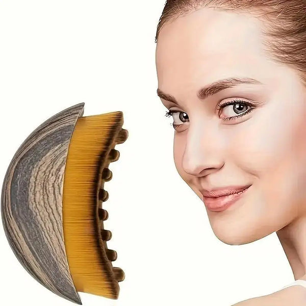 A close-up of a natural-bristle face brush showing its curved shape and golden bristles against a light skin tone.