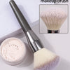 An oversized multi-purpose makeup brush with a silver handle and fluffy pink bristles is shown next to its powder container.