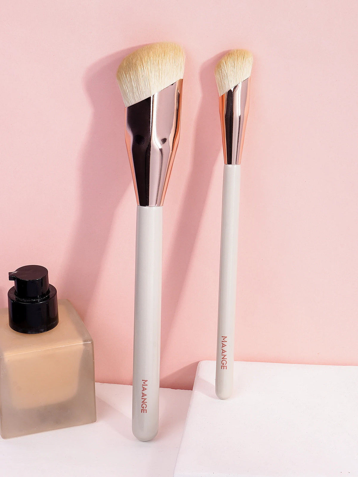 A set of two natural-bristled makeup brushes with wooden handles displayed against a pink background.