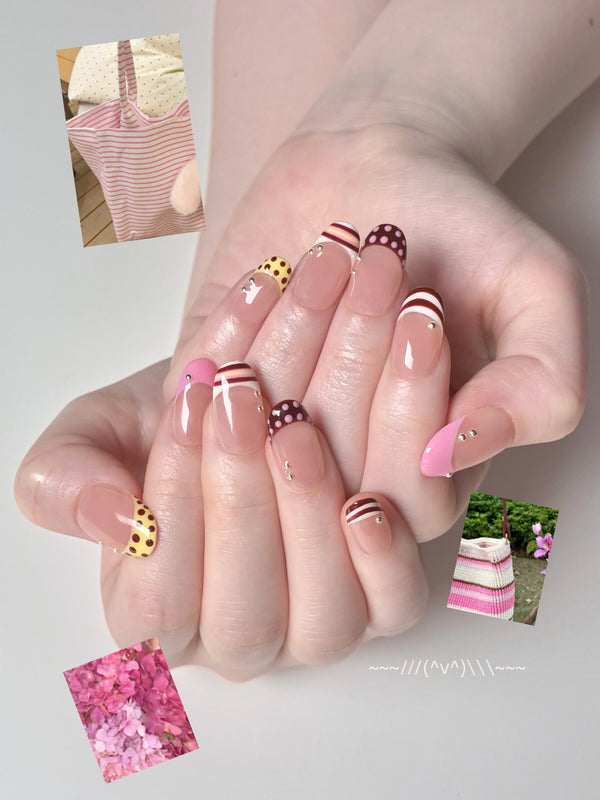 A hand displays pink French manicure press-on nails featuring polka dots and silver bead accents.