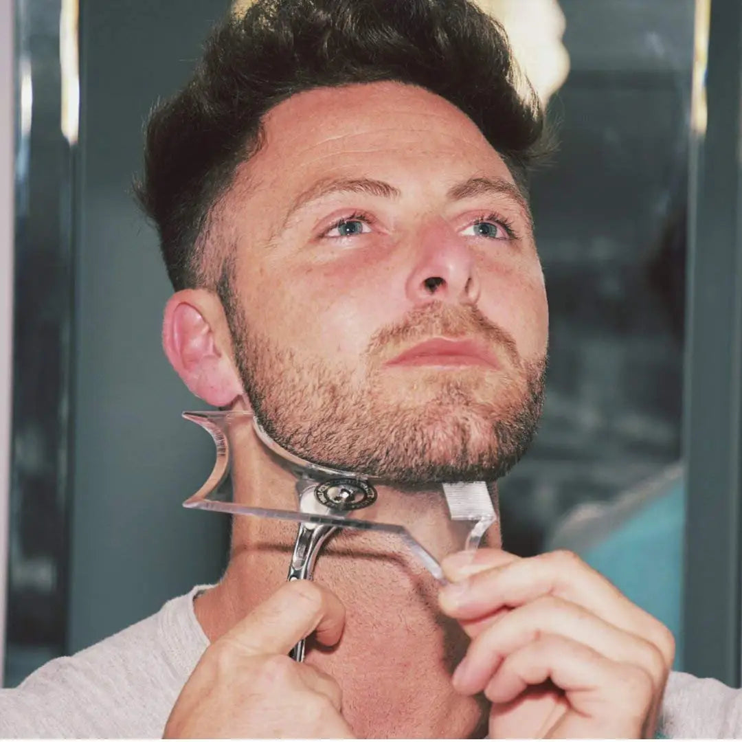 A man is holding an All-in-One Beard Styling Template and Comb against his jawline for grooming.