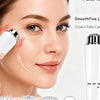 A woman is using a white facial massager device on her face, with various interchangeable silicone tips displayed nearby.
