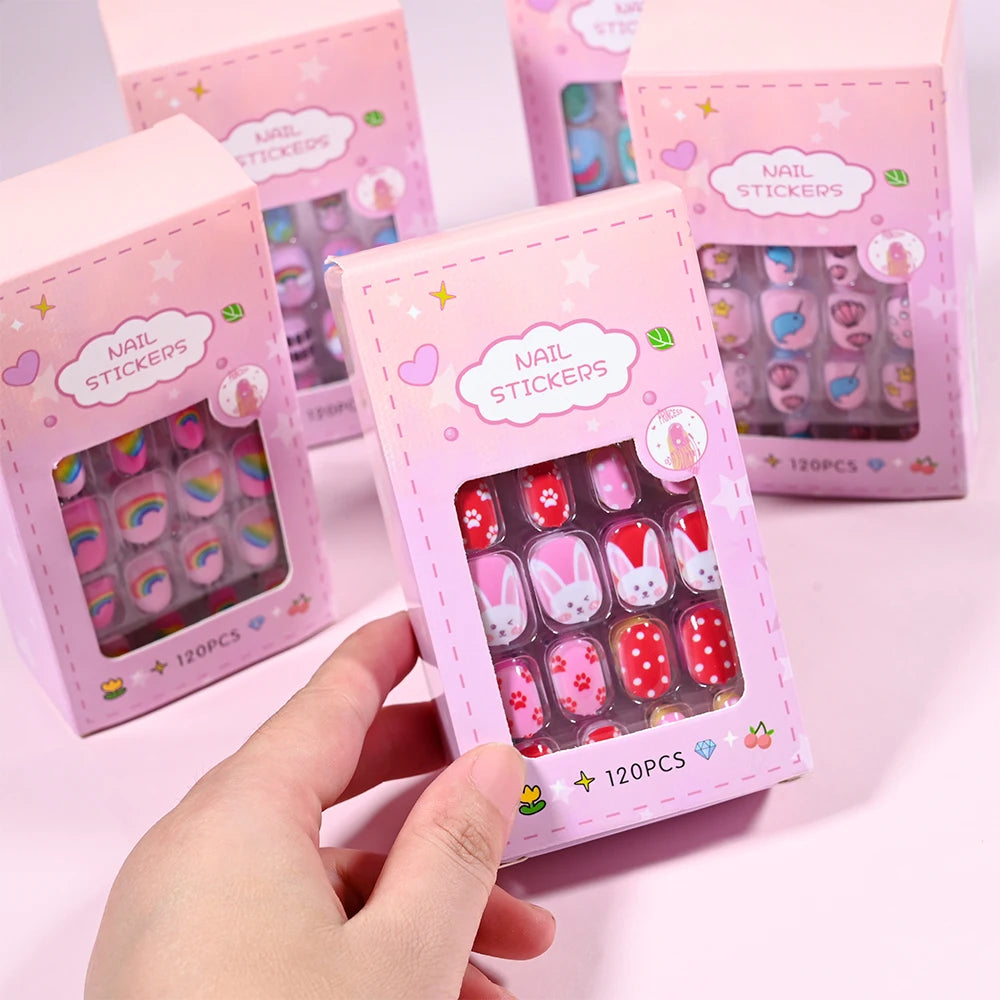 Una mano sostiene una caja de uñas postizas de presión para niños de 120 piezas en empaque rosa.