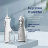 A white portable oral irrigator device with a large screen and crystal effect is shown on a light gray surface.
