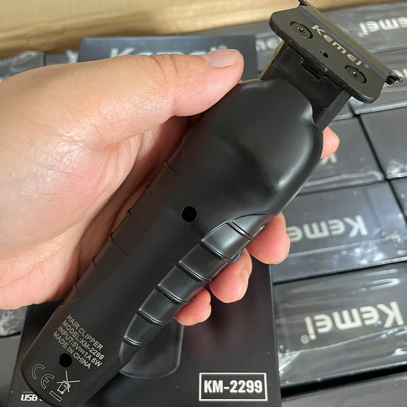 A hand holds a black Kemel KM-2299 electric hair clipper trimmer against a dark background.