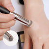 Una mano usa una brocha de maquillaje plateada para aplicar base o corrector en la piel.
