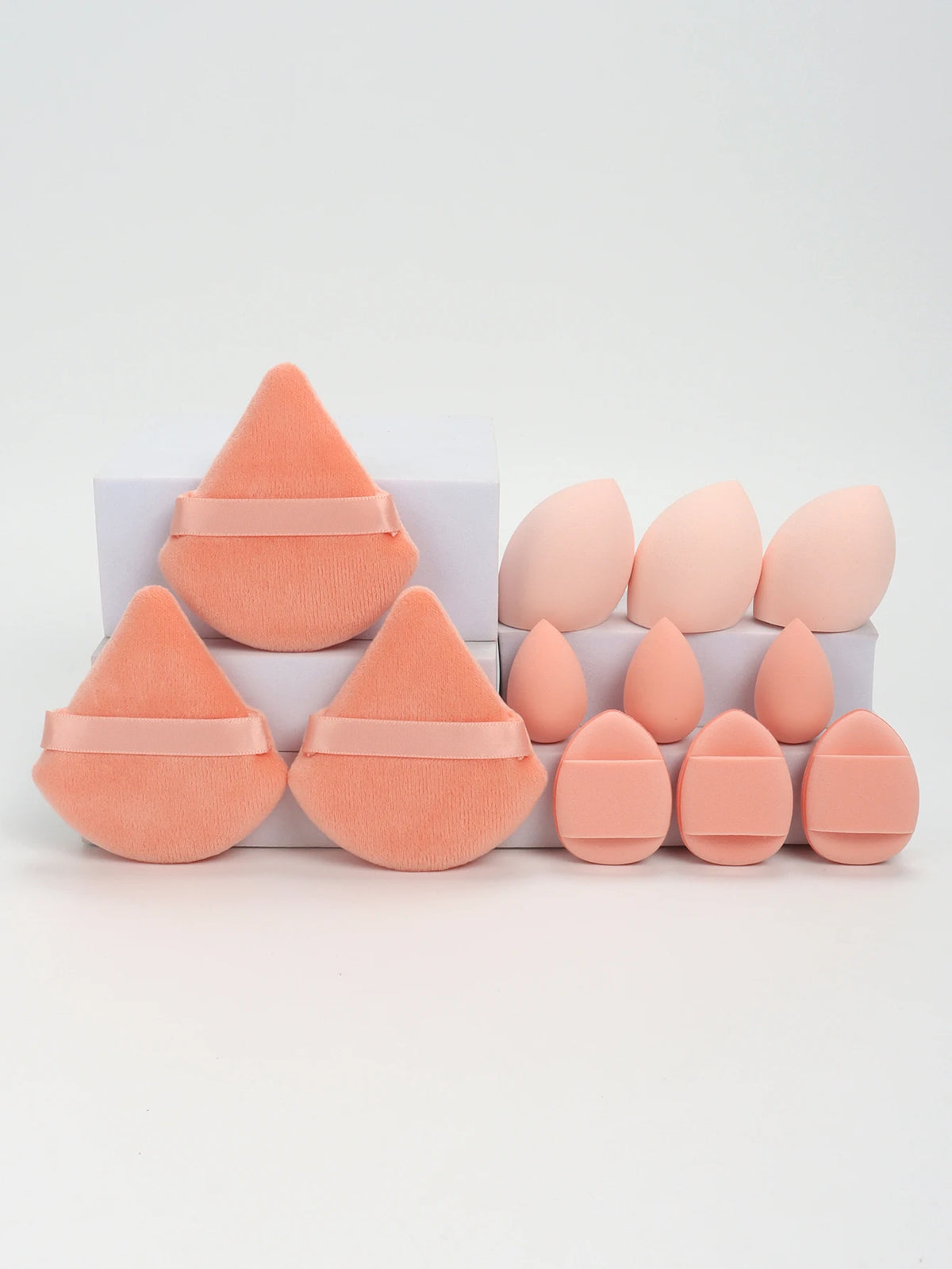 A set of twelve peach-colored makeup sponges in various cone and oval shapes displayed on a white surface.