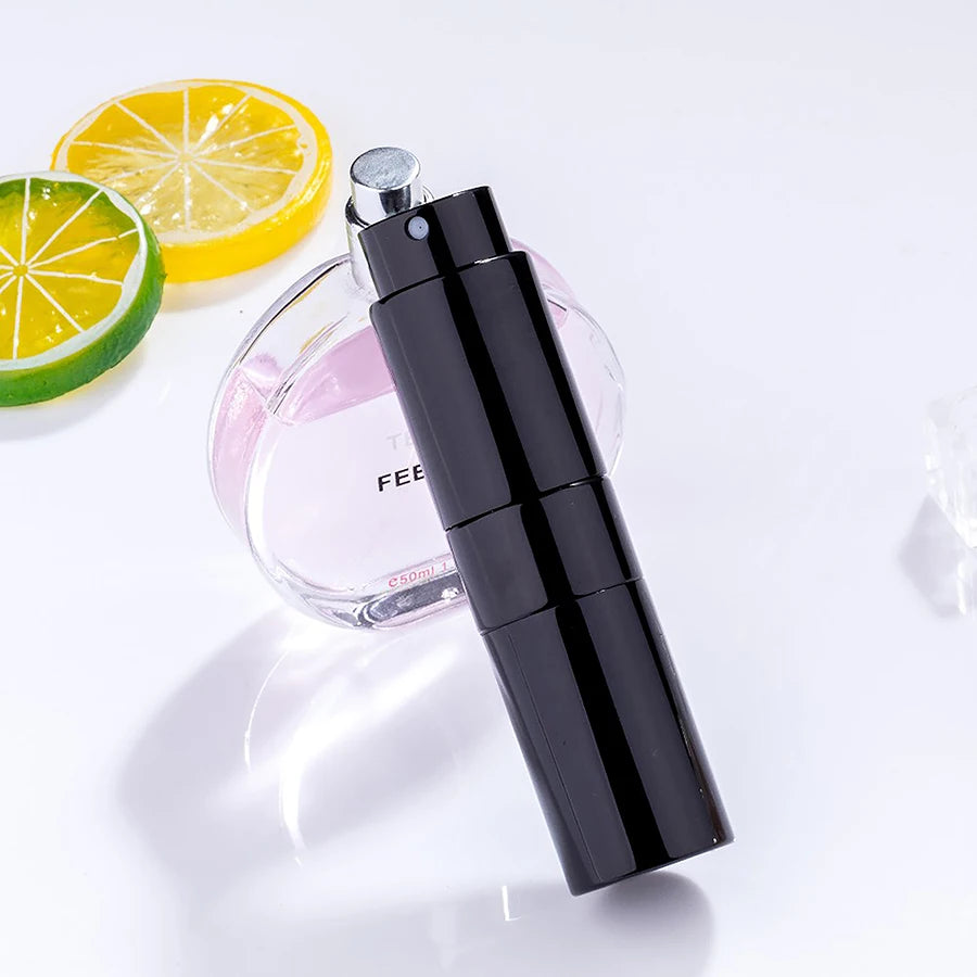 Flacon d'eau de parfum noir à côté d'une tranche de citron et d'un lime, sur fond blanc.