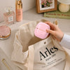 A hand is holding a pink portable hair straightener inside a beige Arles fabric bag.