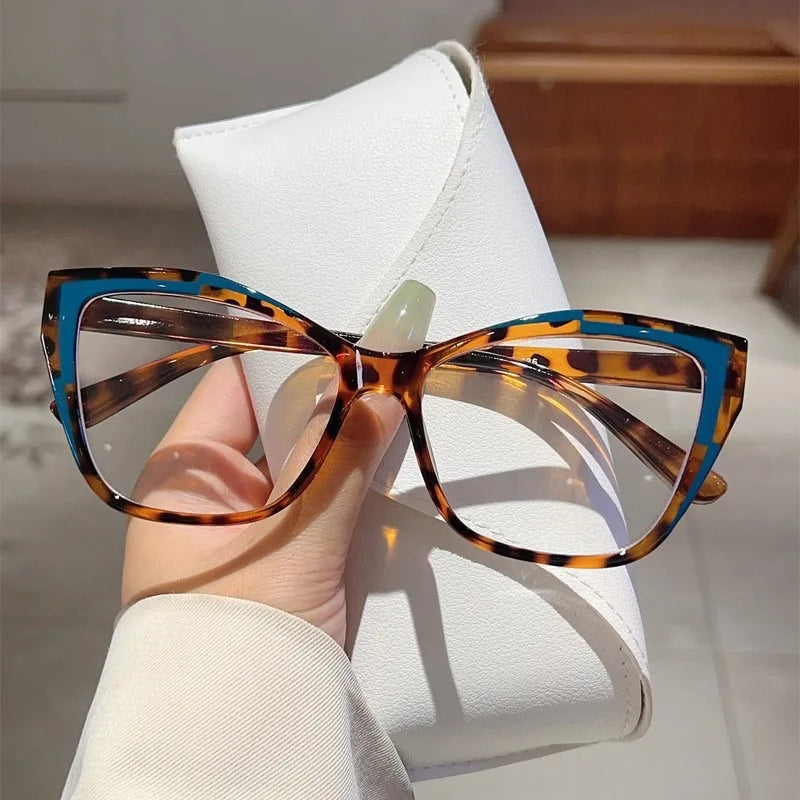 Une paire de lunettes de lecture en forme de œil de chat tortois avec des accents bleus posées sur une étui en cuir blanc.