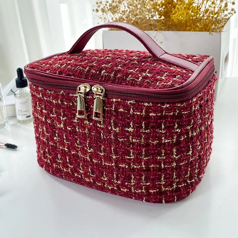 A deep red knitted canvas makeup pouch with a pink trim and gold zippers resting on a white surface.