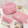 Pink quilted cotton makeup bag with a red floral pattern displayed next to a white lamp.