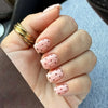 A hand displaying pink and white striped press-on nails on fingers, with a gold ring visible.