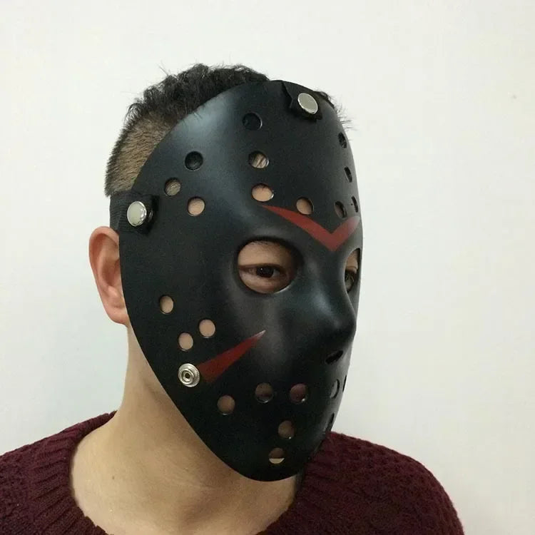 Une personne porte un masque de hockey noir avec des trous et des marques rouges, ressemblant à Jason Voorhees.