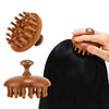 A hand is holding a wooden natural sandalwood therapy massage comb, showing its texture and shape against dark hair.