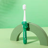 A green dinosaur-themed toothbrush standing upright on a light green surface.