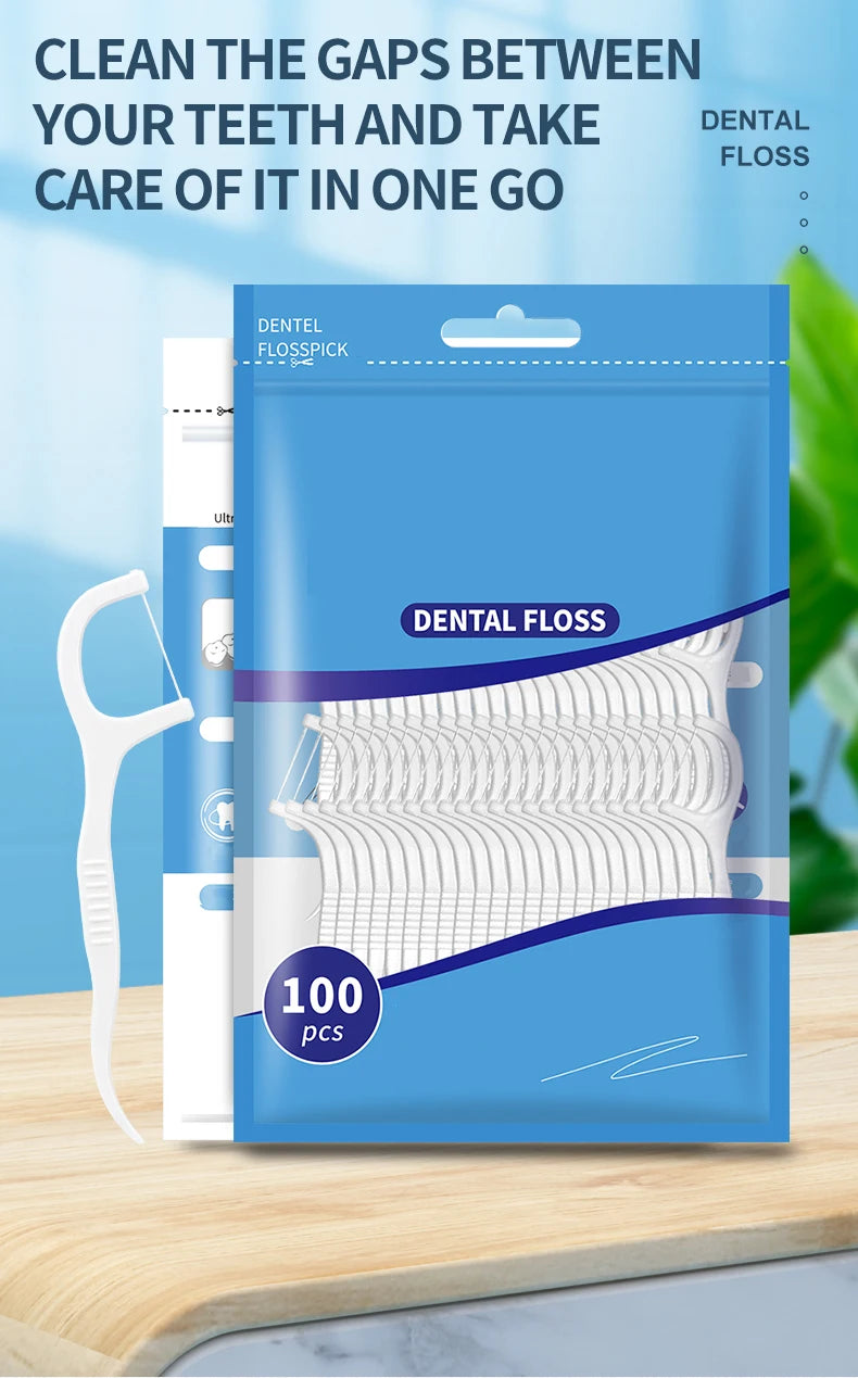 A blue package of dental floss with 100 pieces and a white plastic toothpick shown next to a wooden surface.