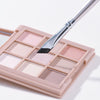 A makeup palette with various shades of pink and nude eyeshadows and an angled eyeliner brush
