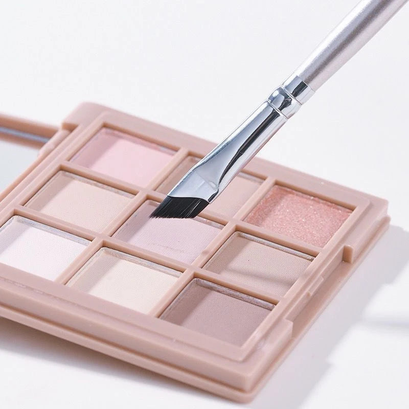 A makeup palette with various shades of pink and nude eyeshadows and an angled eyeliner brush