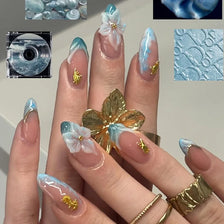 A hand displaying pink cat eye false nails featuring 3D floral and butterfly designs with iridescent blue accents.