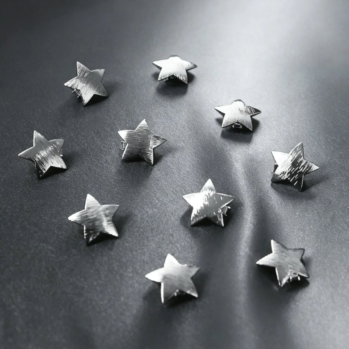 A collection of ten star-shaped hairpins with gold and silver finishes scattered on a dark surface.