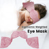 A woman is sleeping with an ergonomic weighted eye mask on her face, resting on white bedding.