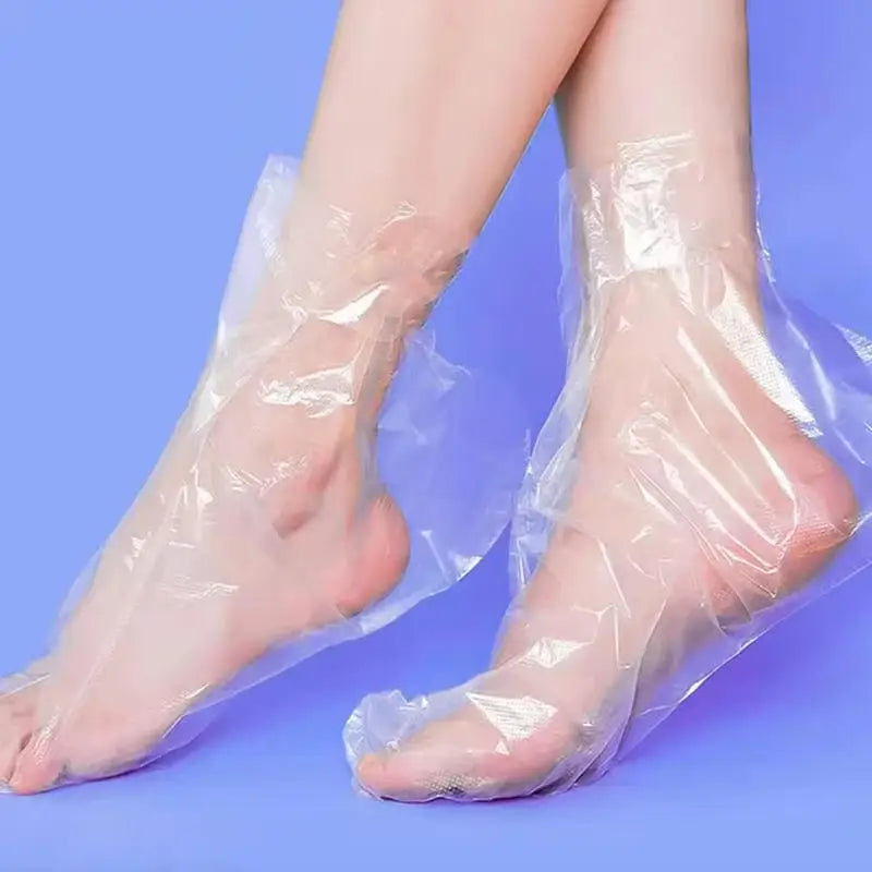 Paire de chaussettes hydratantes jetables transparentes portées sur les pieds d'une personne.