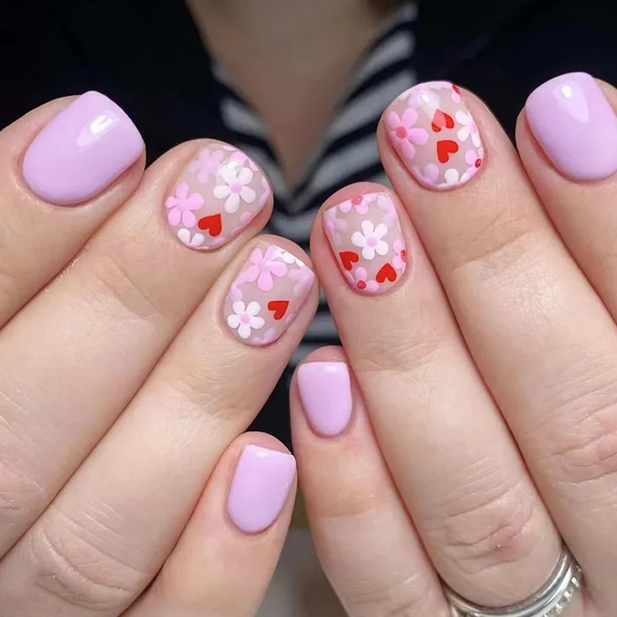 Close-up of hands displaying a set of press-on acrylic nails with pink and red floral designs