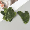 A set of natural jade gua sha tools in a vibrant green color are displayed on a light surface.
