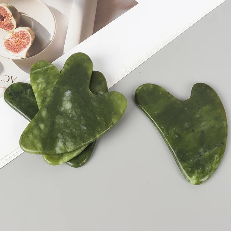A set of natural jade gua sha tools in a vibrant green color are displayed on a light surface.