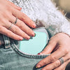 A person's hands are holding a portable LED magnifying makeup mirror against a denim jacket.