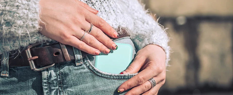 A person's hands are holding a portable LED magnifying makeup mirror against a denim jacket.