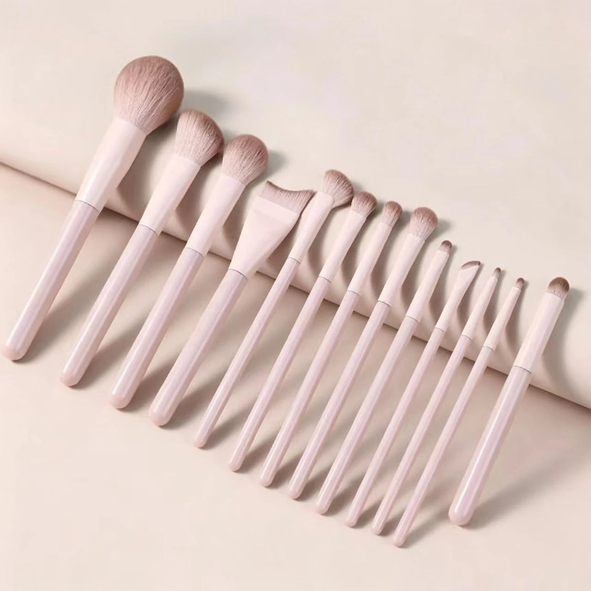 A set of professional loose powder makeup brushes with light pink handles and natural hair bristles arranged diagonally.