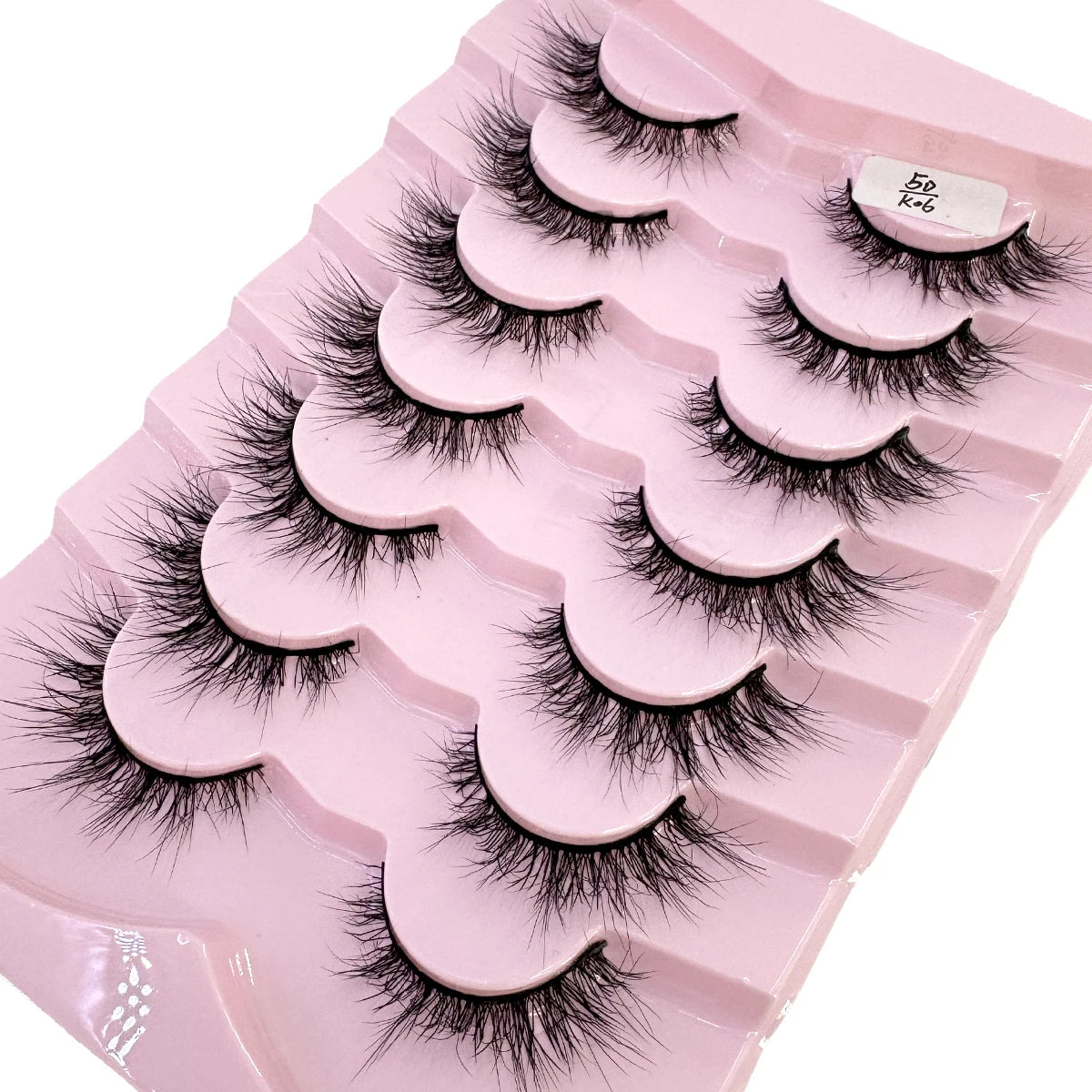 Plateau en plastique rose contenant divers styles de faux cils de renard noirs pour maquillage.