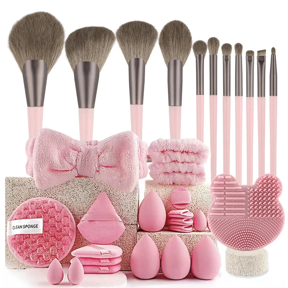 A set of pink and beige professional makeup brushes, sponges, and applicators displayed on a wooden surface.