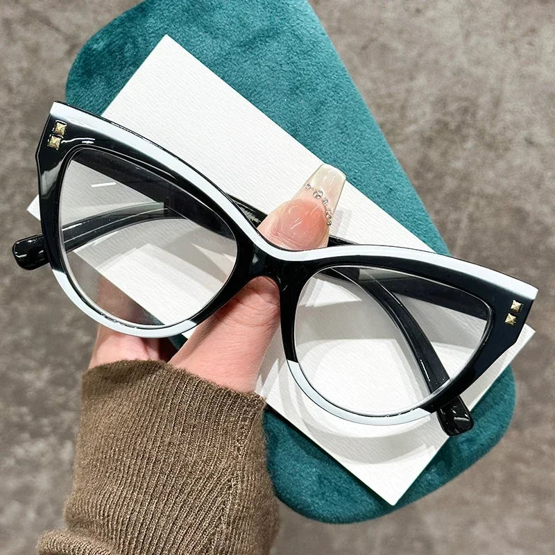 Une paire de lunettes de lecture pour chats noires avec des accents argentés posées sur un tissu bleu sarcelle.