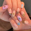 A hand displays a set of press-on false nails featuring pink and brown polka dots and ladybug designs on an almond shape.