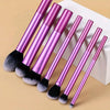 A set of seven professional makeup brushes with long, slender handles and fluffy brush heads in a metallic pink color.