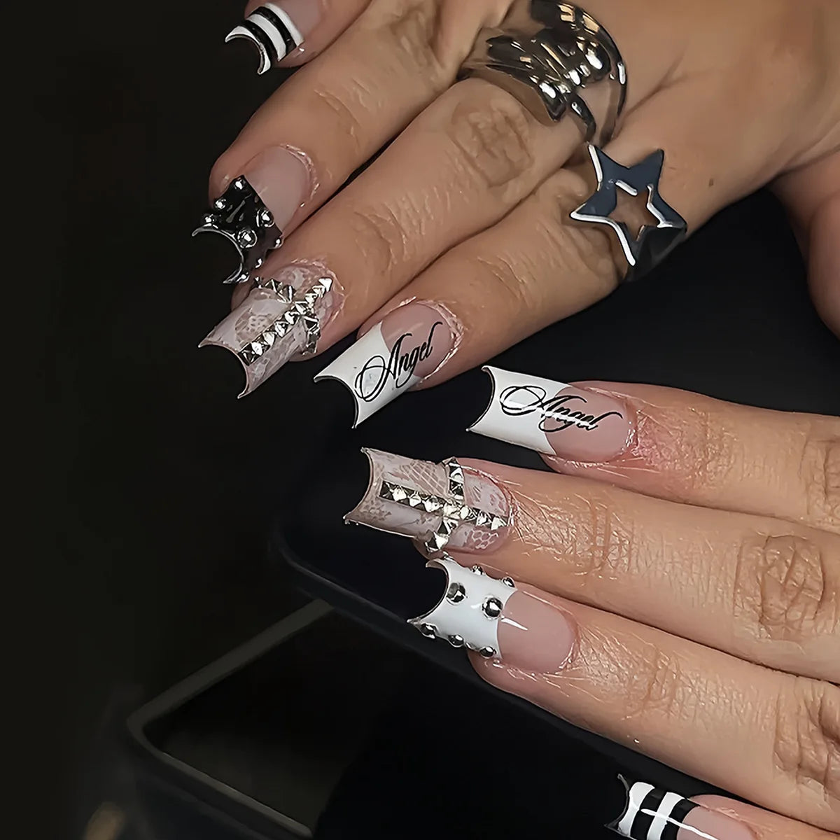 A close-up of a hand displaying gothic Y2K press-on nails featuring silver cross and bow designs.