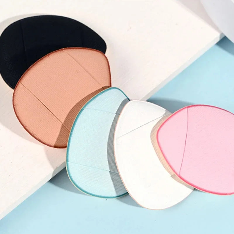 Un set de cinq mini éponges de fondation aux couleurs variées : noir, pêche, vert menthe, blanc et rose, posés sur un fond cl