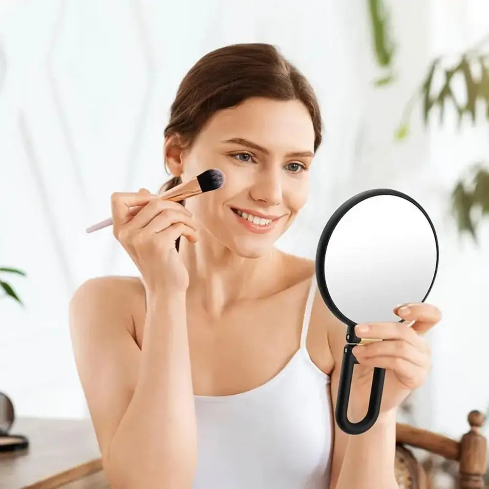 Une femme utilise un miroir de voyage à double face pour vérifier sa peau dans un intérieur lumineux.