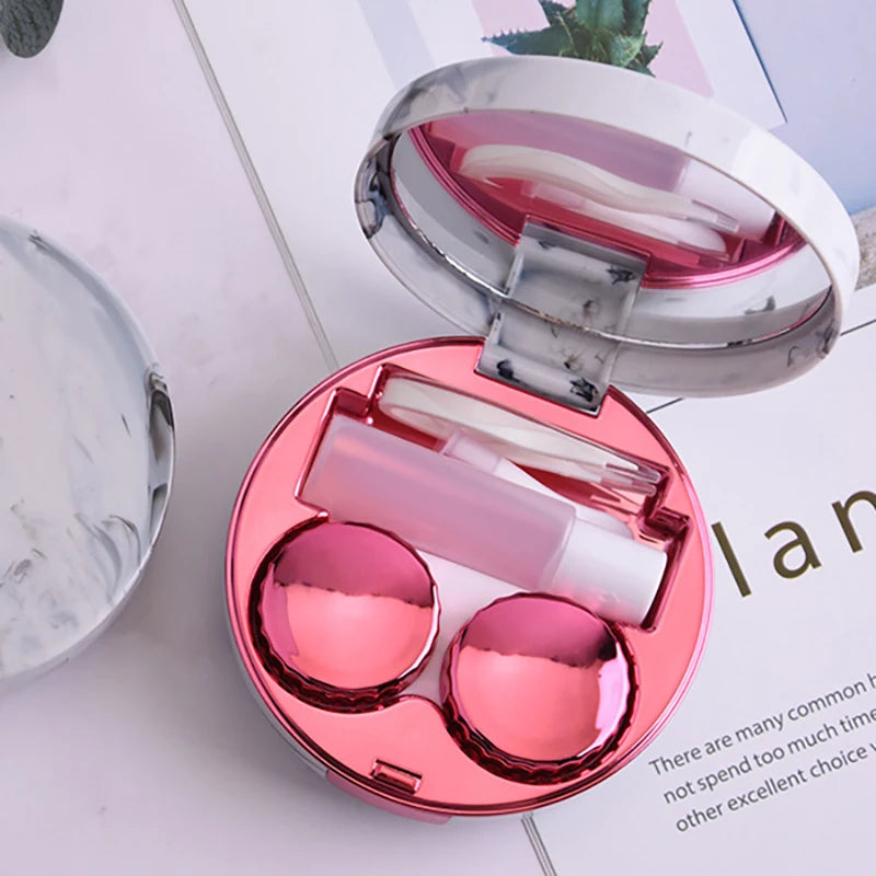 A pink round marble pattern contact lens storage box open to show clear contact lenses inside.