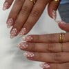 Close-up of hands displaying light pink and white polka dot press-on nails with gold jewelry.