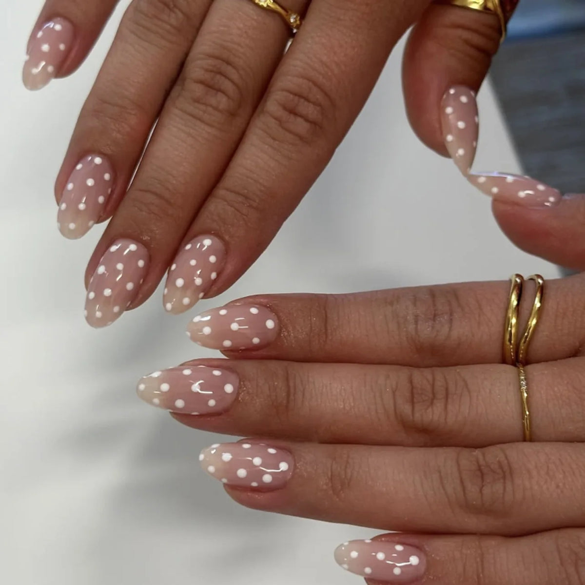 Close-up of hands displaying light pink and white polka dot press-on nails with gold jewelry.