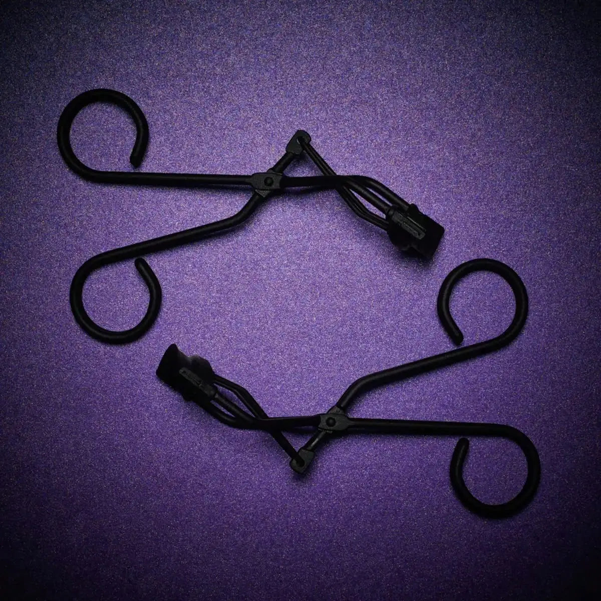 A black metal eyelash curler is shown against a purple background.