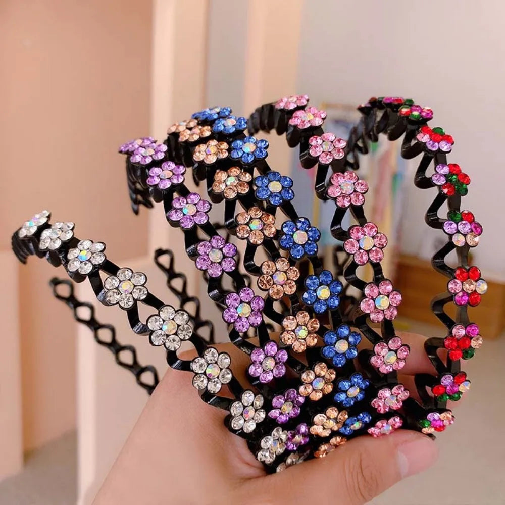 A hand holds a black rhinestone wave headband decorated with colorful floral stones.