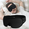Un hombre duerme con una máscara de dormir ergonómica negra en los ojos, sobre ropa de cama blanca.