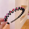 A black rhinestone wave headband decorated with colorful gems is held by a hand.