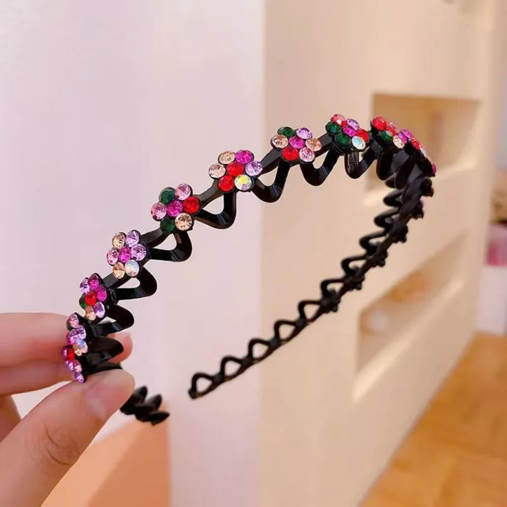 A black rhinestone wave headband decorated with colorful gems is held by a hand.