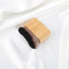 A wooden-handled makeup brush with dark bristles resting on a white satin fabric.